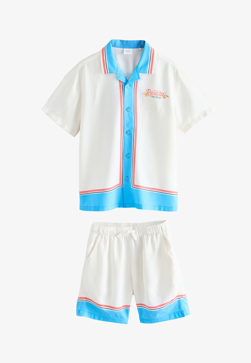 Camisa blanca de manga corta y pantalones cortos a juego con ribetes azules y rojos, con cierre de botones y texto "Riviera" en el pecho.