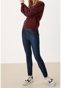 Tmavě modré skinny džíny s kontrastním prošíváním, spárované s vínově červeným texturovaným svetrem a bílými, námořnickými a červenými sportovními teniskami.