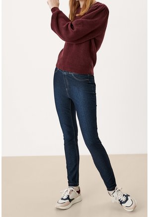 Tmavě modré skinny džíny s kontrastním prošíváním, spárované s vínově červeným texturovaným svetrem a bílými, námořnickými a červenými sportovními teniskami.