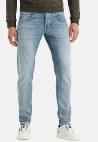 Hellblaue Jeans im geraden Schnitt mit frontalen Taschen und subtilen Verblassungen. Kombiniert mit weißen Turnschuhen.