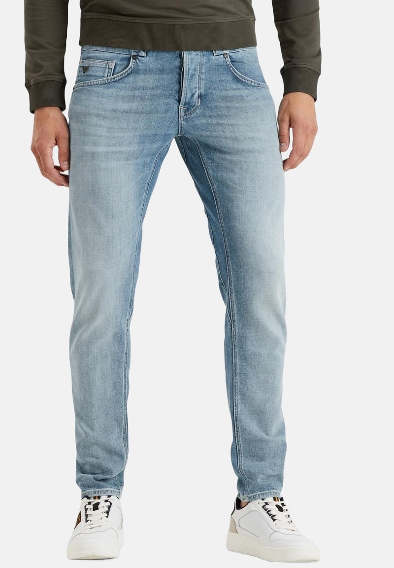 Hellblaue Jeans im geraden Schnitt mit frontalen Taschen und subtilen Verblassungen. Kombiniert mit weißen Turnschuhen.