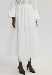 Witte tule rok tot de knie met een elastische tailleband, gelaagd ontwerp en lichte textuur. Gemaakt om te dragen met zwarte puntige hakken.