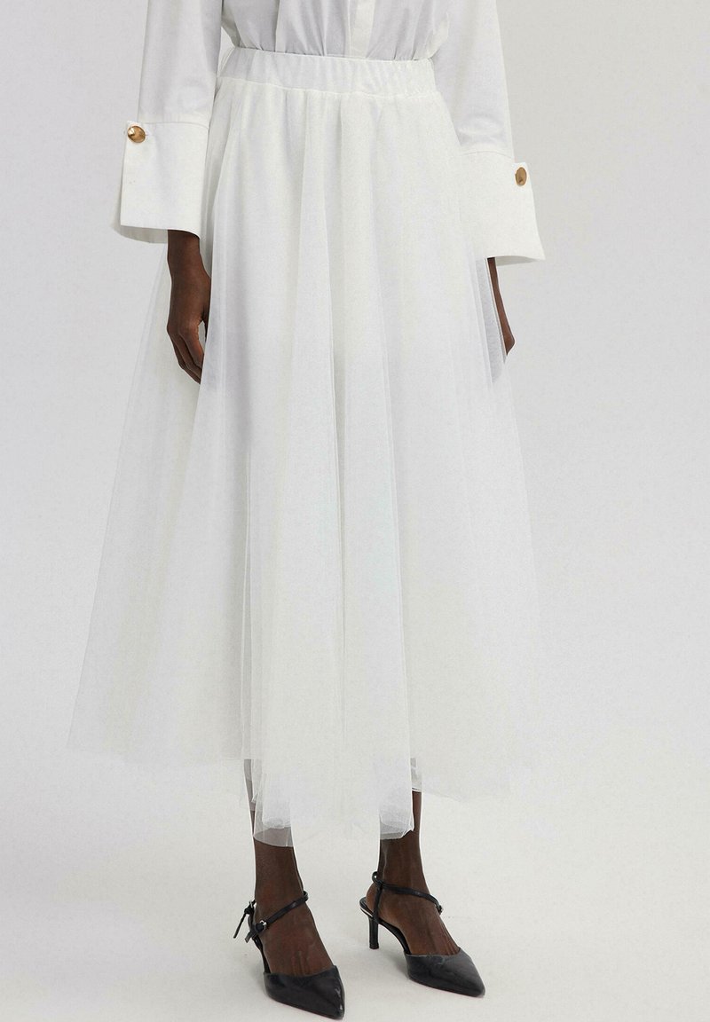 Witte tule rok tot de knie met een elastische tailleband, gelaagd ontwerp en lichte textuur. Gemaakt om te dragen met zwarte puntige hakken.