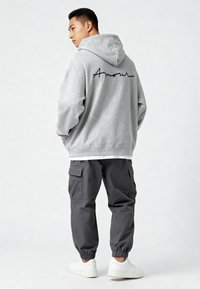 Felpa grigia con la scritta "Amour" stampata in nero sulla schiena. Abbinata a pantaloni cargo grigi scuri e sneakers bianche. Taglio e design casual.