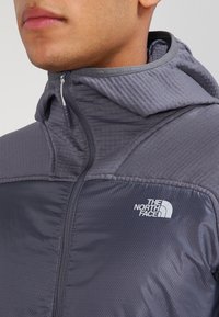 Grå, lättviktsjacka med dragkedja, justerbar huva, strukturerad tyg och The North Face-logotyp på bröstet.