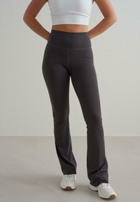 Leggings évasés taille haute de couleur gris foncé, fabriqués dans un tissu extensible, avec une texture lisse et des détails de couture minimaux.