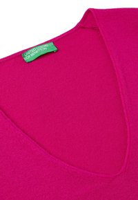 Fuksjowy sweter w serek o gładkiej fakturze, wykonany z dzianiny. Zawiera zieloną metkę marki, wykończenia szwów oraz minimalistyczny design.