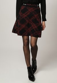 Roter und schwarzer Karottenrock mit einem elastischen Bund, der mit gestickten Herzen verziert ist, ausgestelltes Design, aus strukturiertem Stoff hergestellt.