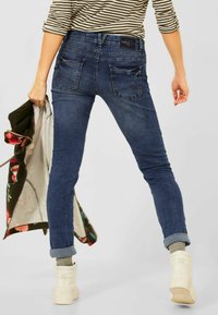 Blå slim jeans med medelhög midja, med bakfickor och en lätt tvätt, bärs med en randig topp och vita ankelskor.