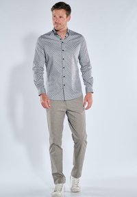 Grau gemusterte Hemd mit Kragen, kombiniert mit hellgrauen Hosen und weißen Sneakers, auf einem Model vor einem schlichten Hintergrund.