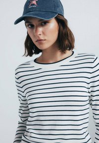 Camicia bianca a maniche lunghe con righe blu navy e colletto a coste, abbinata a un berretto blu navy con un design a stella rossa e bianca.