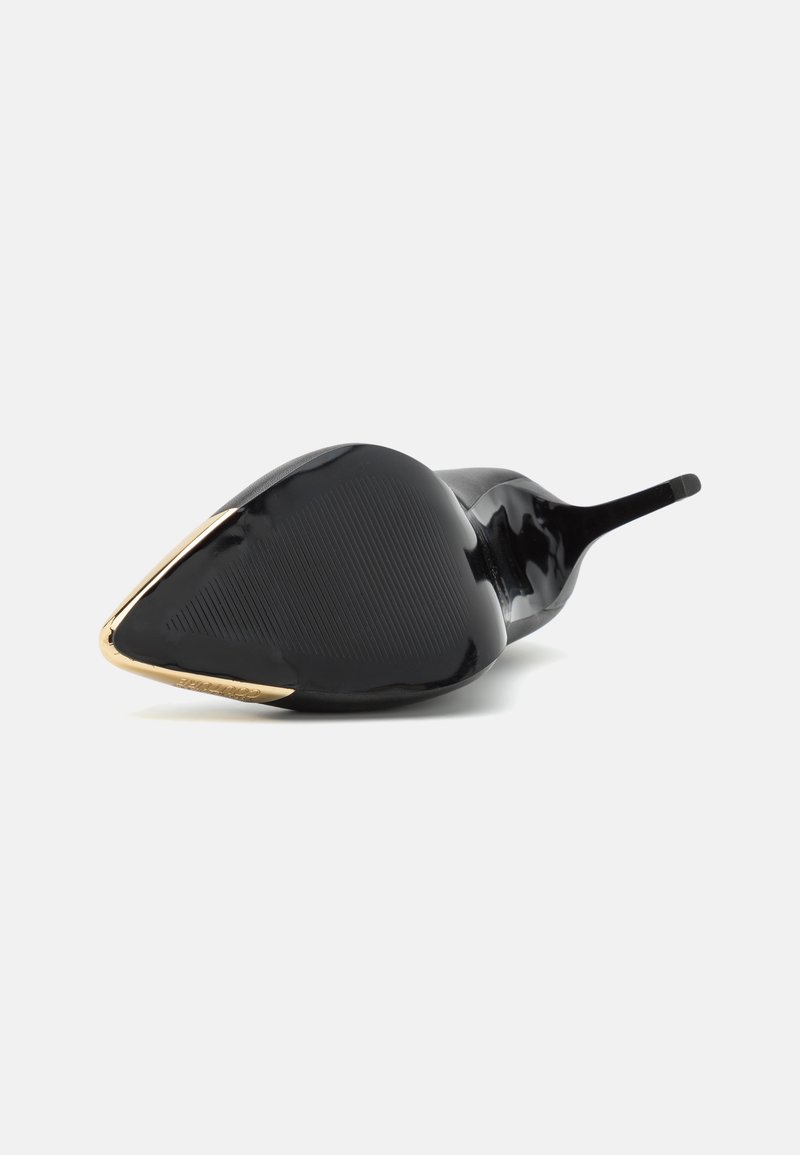 Chaussure à talon haut noire avec un bout pointu, présentant un accent métallisé doré à la pointe et une semelle texturée. Matériau en cuir lisse.