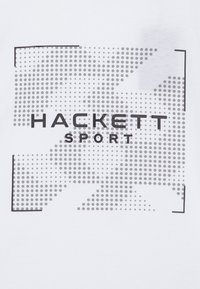 Weißes T-Shirt mit einem grafischen Design, das ein graues gepunktetes Muster und den Text "HACKETT SPORT" in fett schwarzer Schrift zeigt, eingerahmt von einem schwarzen Rechteck.
