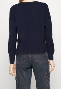 Dunkelblauer Strickpullover mit geripptem Saum und Bündchen, überschnittenen Schultern und einem entspannten Schnitt. Sichtbare Nahtdetails auf dem Rücken.