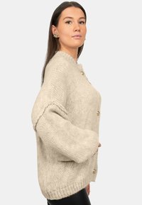 Cardigan lavorato a maglia beige con maniche over, dotato di colletto rotondo e bottoni dorati. Tessuto testurizzato e vestibilità rilassata.