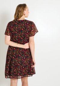 Robe noire à manches courtes avec un motif géométrique multicolore, dotée d'un tissu léger et transparent et d'un ourlet évasé.
