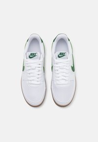 Białe trampki z zielonymi akcentami, z teksturowaną cholewką, płaskimi sznurowadłami i podeszwą z gumy. Logo Nike na języku i boku.