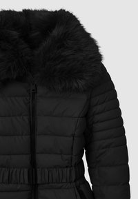 Giacca a piumino nera con colletto in pelliccia sintetica, design trapuntato e vita stretta. Presenta una chiusura frontale con zip e tasche laterali. Texture liscia.