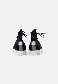 Černé vysoké tenisky s texturovaným povrchem, které mají skvrnitou bílou podrážku, šedé pruhy a malý hvězdicový akcent na patě.