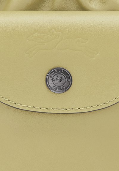 Yellow leather bag with a textured finish, featuring an embossed logo, a circular metallic hardware, and contrasting stitching.