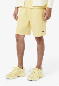 Shorts di cotone gialli con tasche e logo ricamato; abbinati a sneakers gialle con dettagli in rete e suole in gomma.