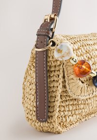 Sac à main en paille tressée avec bandoulière en cuir marron et grosses perles décoratives marbrées et couleur ambre attachées à un anneau doré.
