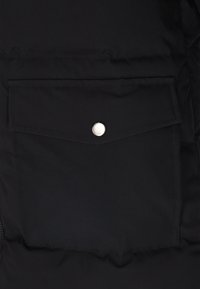 Giacca a vento nera con una tasca frontale e chiusura a pulsante a pressione argentato. Il materiale appare liscio con una finitura opaca.