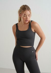 Svart ribbet crop top og høy midje leggings laget av elastisk stoff. Har en tettsittende design med rund hals og minimal logo-detalj.
