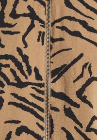 Gros plan d’un tissu marron avec un motif de rayures de tigre noires et une fermeture éclair métallique centrale.