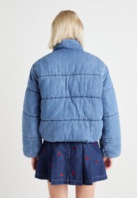 Light blue denim puffer jacket with horizontal stitching and a high collar. Worn over a dark blue skirt with red bow patterns.