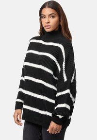 Sweater in bianco e nero a righe, oversize, con collo alto, texture a maglia e maniche larghe. Presenta audaci righe orizzontali.