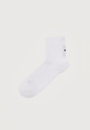 Chaussette blanche unique pour la cheville avec un petit logo noir sur le côté, posée à plat sur un fond neutre.