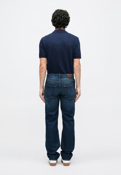 Μπλε πουκάμισο τύπου πόλο σε σκούρο μπλε χρώμα συνδυασμένο με τζιν παντελόνι σε μπλε ντένιμ, με άνετη εφαρμογή, εμφανή ραφές και καφέ δερμάτινο ταμπελάκι στη μέση.