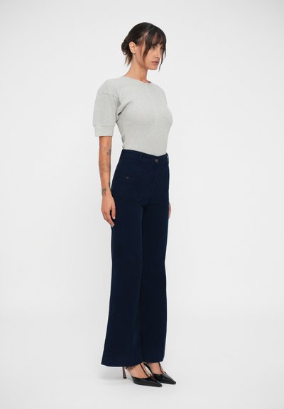 Pulover gri ajustat cu mâneci scurte, asortat cu pantaloni neagră cu talie înaltă și laturi largi. Modelul poartă pantofi negri cu vârf ascuțit.