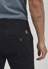 Pantaloni negri din bumbac, cu un buzunar la spate dotat cu închidere pe buton și o etichetă din piele maro. Textură netedă, croi casual.