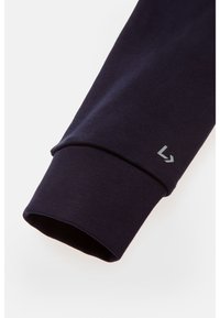 Poignet de chemise à manches longues bleu marine avec texture côtelée ; comporte un petit détail de logo gris près du poignet. Matière en mélange de coton.