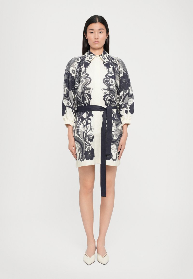 Rochie albă cu imprimeu floral bleumarin, sleeve bufante și o curea în talie. Pantofi cu vârf ascuțit, crem. Material neted cu o siluetă ajustată.