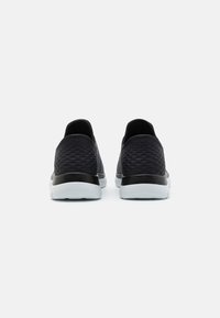 Scarpe sportive nere con una tomaia texturizzata, colletto imbottito e suola bianca a contrasto. Presentano un design liscio e aerodinamico.