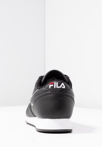 Scarpa atletica nera con tomaia a trama liscia, suola bianca, logo Fila sul tallone e collo imbottito per supporto. Vista posteriore.