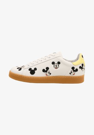 Biały sneaker z brązową podeszwą, ozdobiony wieloma czarno-białymi kreskówkowymi twarzami myszy i żółtą pętelką na pięcie.