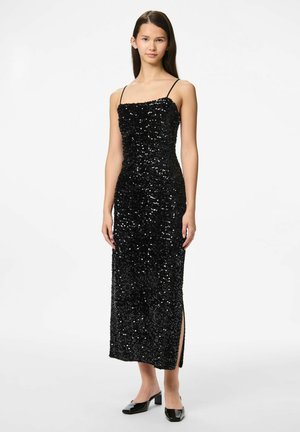 Crna haljina sa šljokicama, tankim trakama, prilagođenim korzetom i bočnim prorezom, upotpunjena sjajnim crnim cipelama na blok-petama. Glatka tekstura.