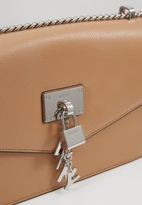 Torebka skórzana w kolorze brązowym z srebrnym ła�ńcuszkiem, detalem z zamkiem oraz logo DKNY. Gładka tekstura z przeszyciami i elegancki design.