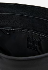 Schwarzes Leder-Tote-Interior mit glatter Textur, ausgestattet mit einer Reißverschlusstasche und einem kleinen schwarzen Lederschild. Minimalistisches Design.