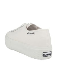 Sneaker bianco in tela con suola in gomma, punta rotonda, sei asole e un'etichetta con il marchio sul tallone. Suola testurizzata per una migliore aderenza.