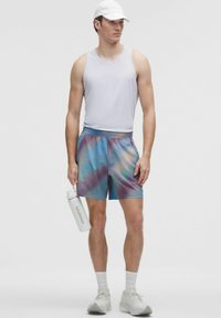 Conjunto atlético para hombres que incluye una camiseta sin mangas blanca, unos pantalones cortos de tie-dye multicolores y una botella de agua blanca con la etiqueta "lululemon".