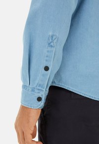 Lichtblauwe denimshirt met knoopmanchetten, voorzien van zwarte ronde knopen en contrasterende stiksels. Gladde textuur met een casual pasvorm.