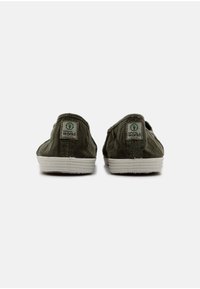 Zöld vászon slip-on cipők fehér gumitalppal, hátul logóval. A dizájn egyszerű és alacsony profilú.