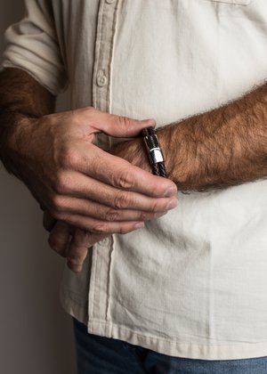 Leather bracelet in braided dark brown with a silver clasp detailing; worn on a wrist with visible texture and hands.