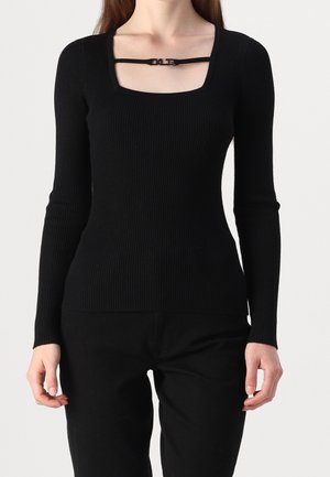 Femme portant un haut noir côtelé ajusté à manches longues avec un décolleté carré et un détail de fine sangle à boucle sur la poitrine.