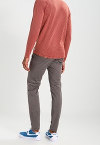 En figurnära, långärmad, röd texturerad skjorta kombinerad med grå slim-fit byxor och blå sneakers. Märkbara kontrasterande vita detaljer på skorna.